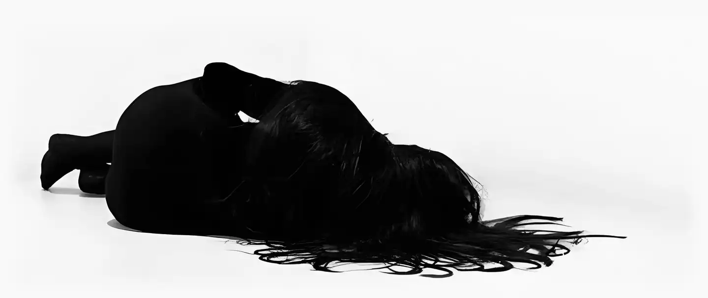 Silhouette of a woman lying on a white studio floor, her hair spread across it